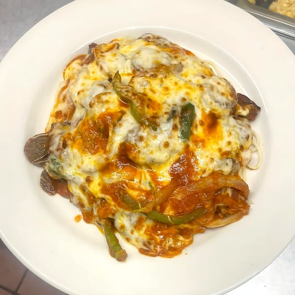 Baked spaghetti with melted cheese, tomato sauce, green peppers, and mushrooms on a white plate.