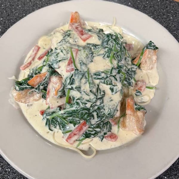 Creamy pasta with spinach, red peppers, and shrimp on a white plate.