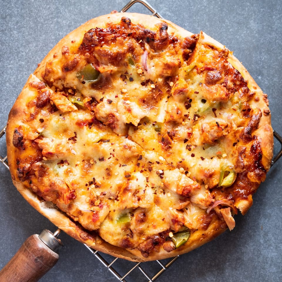 A freshly baked Sammy's Italian chicken pizza with melted cheese, green peppers, and red pepper flakes.