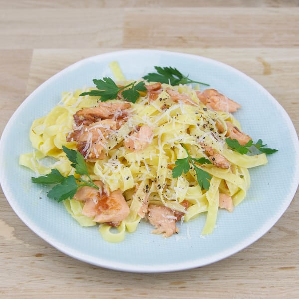Fettuccine pasta with salmon, parmesan cheese, black pepper, and parsley on a light blue plate.