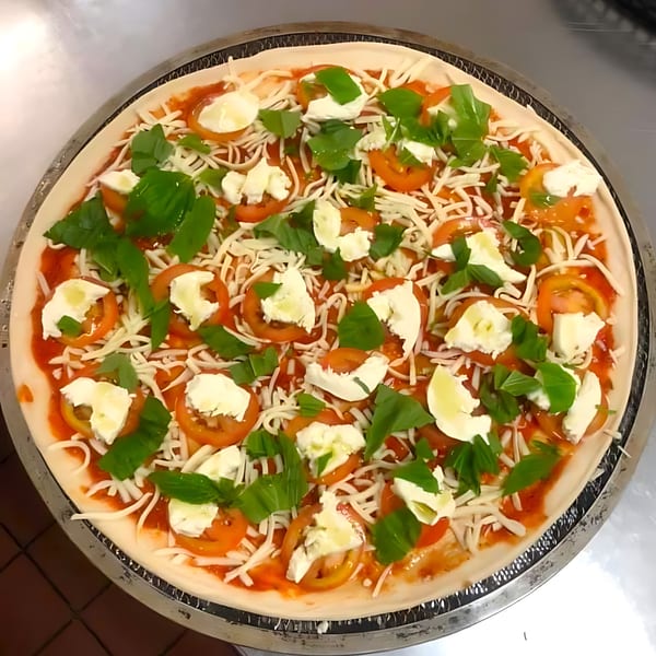 Uncooked Sammy's Italian pizza with tomato sauce, mozzarella, sliced tomatoes, and fresh basil.