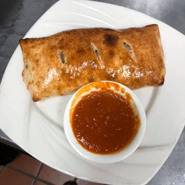 A golden-brown calzone with three slits on top, served with a side of red marinara sauce.