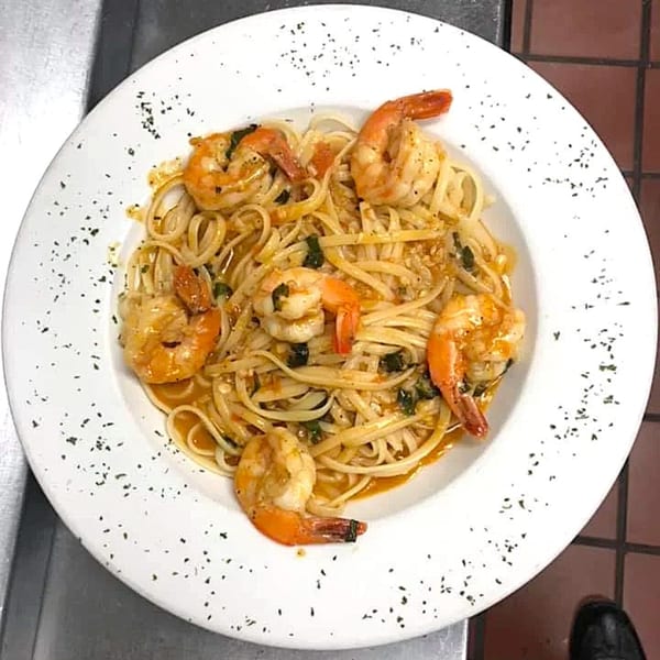 A white plate of Sammy's Italian linguine pasta with shrimp, sauce, and herbs.
