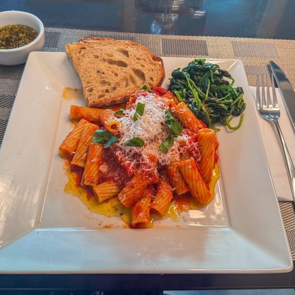 Rigatoni pasta with red sauce, parmesan, and basil, served with bread and spinach.